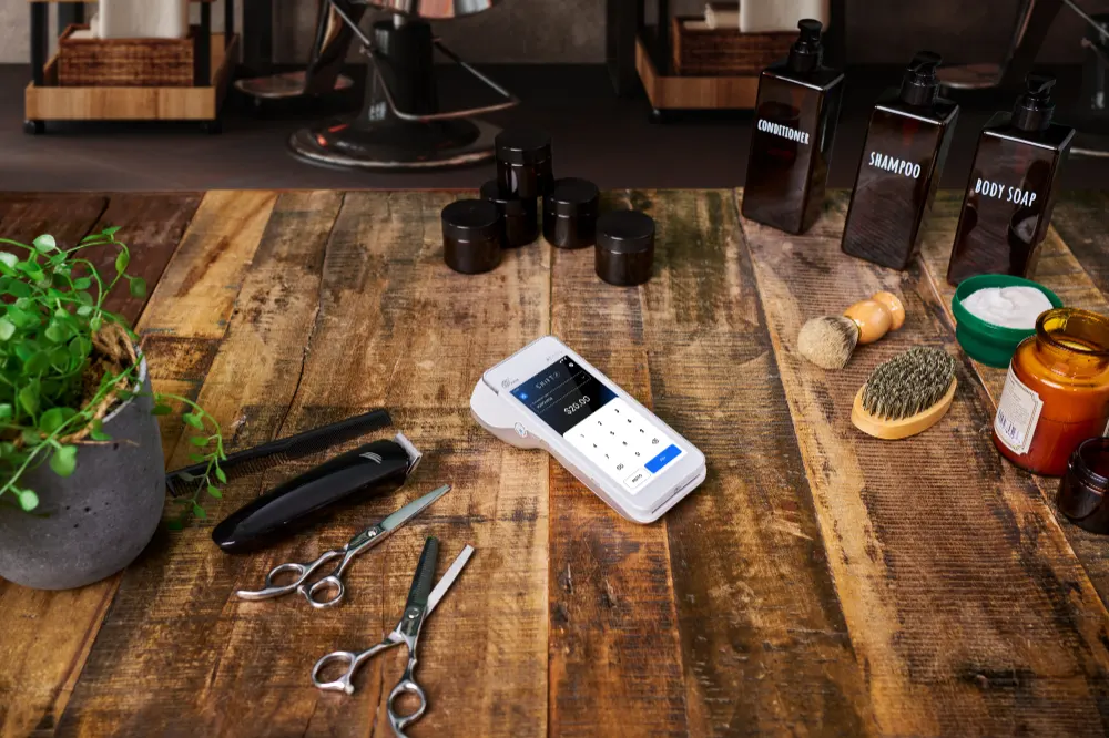 Smartpay Android terminal on wood table surrounding barber tools and accessories