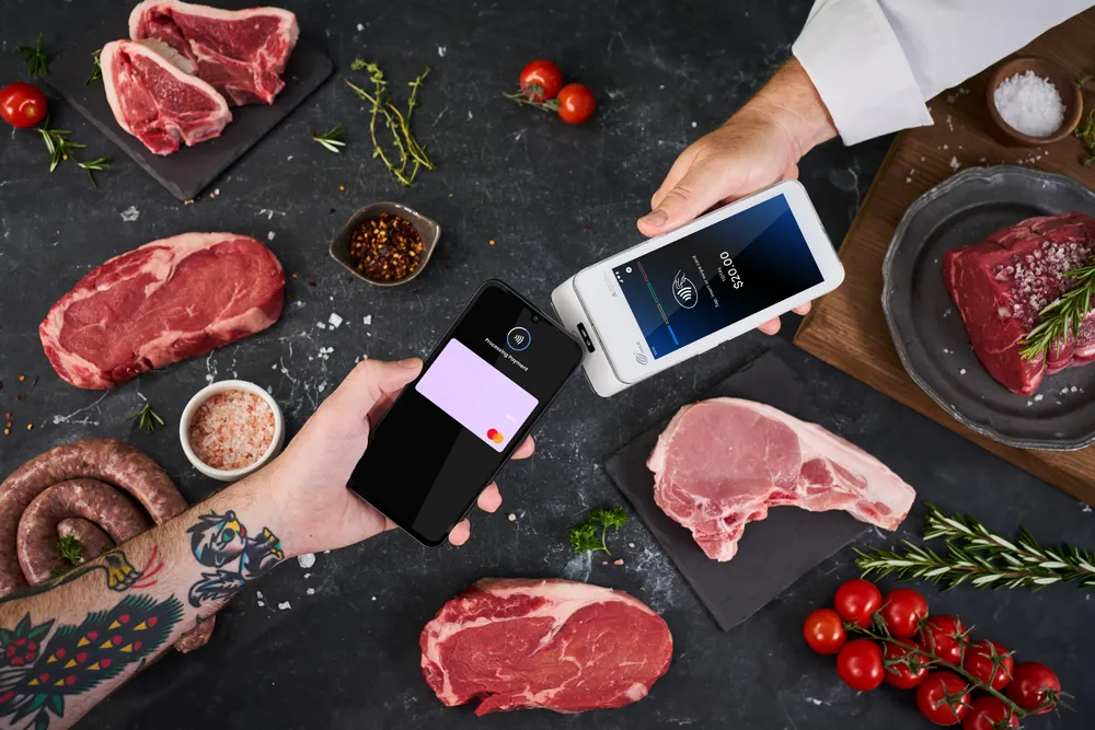 Phone tapping Android terminal to make payment, surrounded by assorted butcher meats